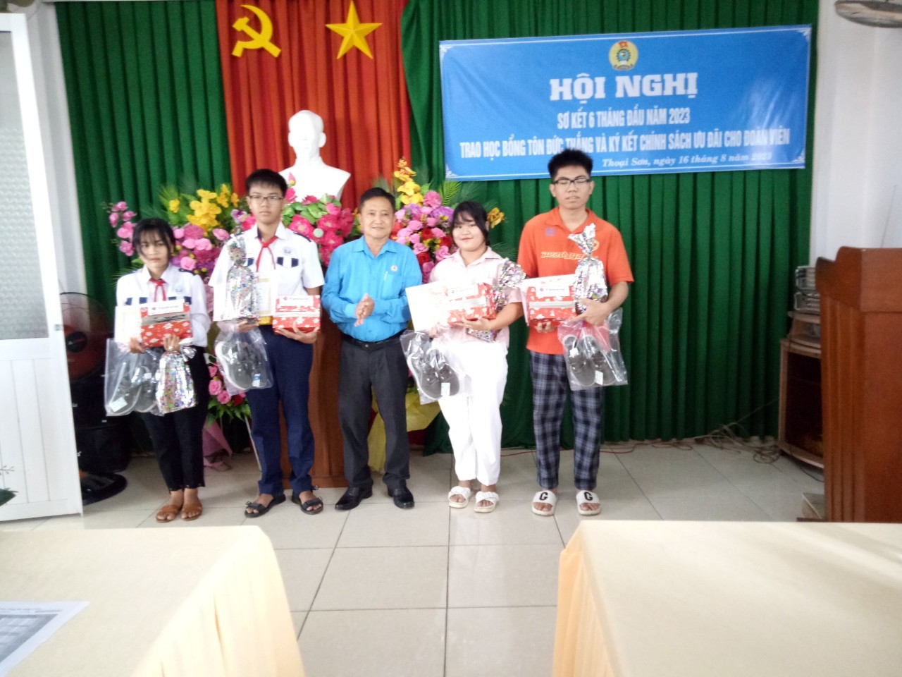 A group of people standing in front of a green and red banner Description automatically generated