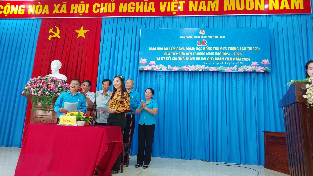 A group of people standing in front of a red table

Description automatically generated